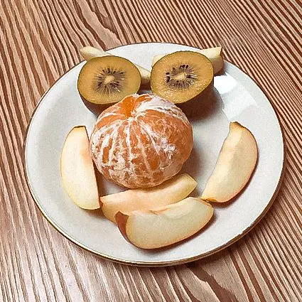 Auf einem Teller Frühstück aus Apfel, gelber Kiwi und Mandarine