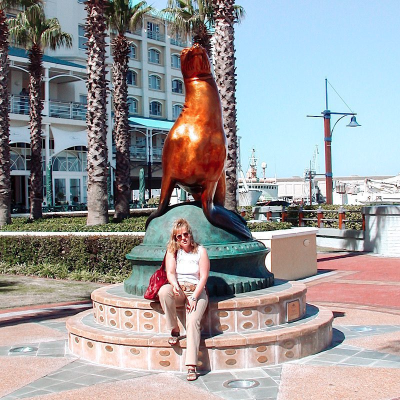 Frau sitzt vor einer Seelöwen Statue 