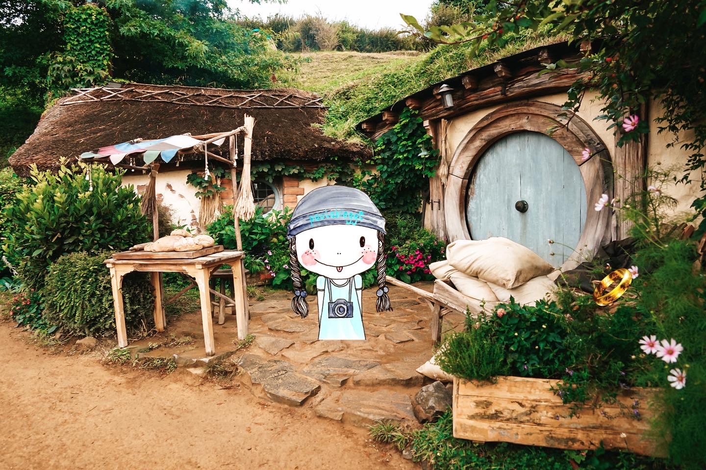 Ein Hobbithaus mit einem Bäcker-Stand davor, eingefügt das Gif Paulabloggt - Mädchen mit Kappe und Fotoapparat 